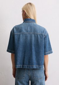 Denim oversized shirt in diepblauw met korte mouwen, een kraag en een rechte onderrand. Heeft contrasterende stiksel en een ontspannen pasvorm.
