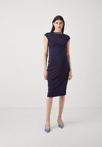 Tamnoplav dres uz tijelo s kratkim rukavima, nabranim detaljima i midi duljinom. Model je kombinirao s svijetloplavim cipelama s ostrim vrhom.