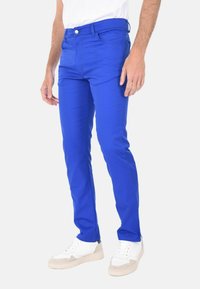 Pantaloni slim-fit in cotone blu, con cinque tasche, chiusura a bottone e dettagli di sbiadimento sottili. Abbinati a sneaker bianche.