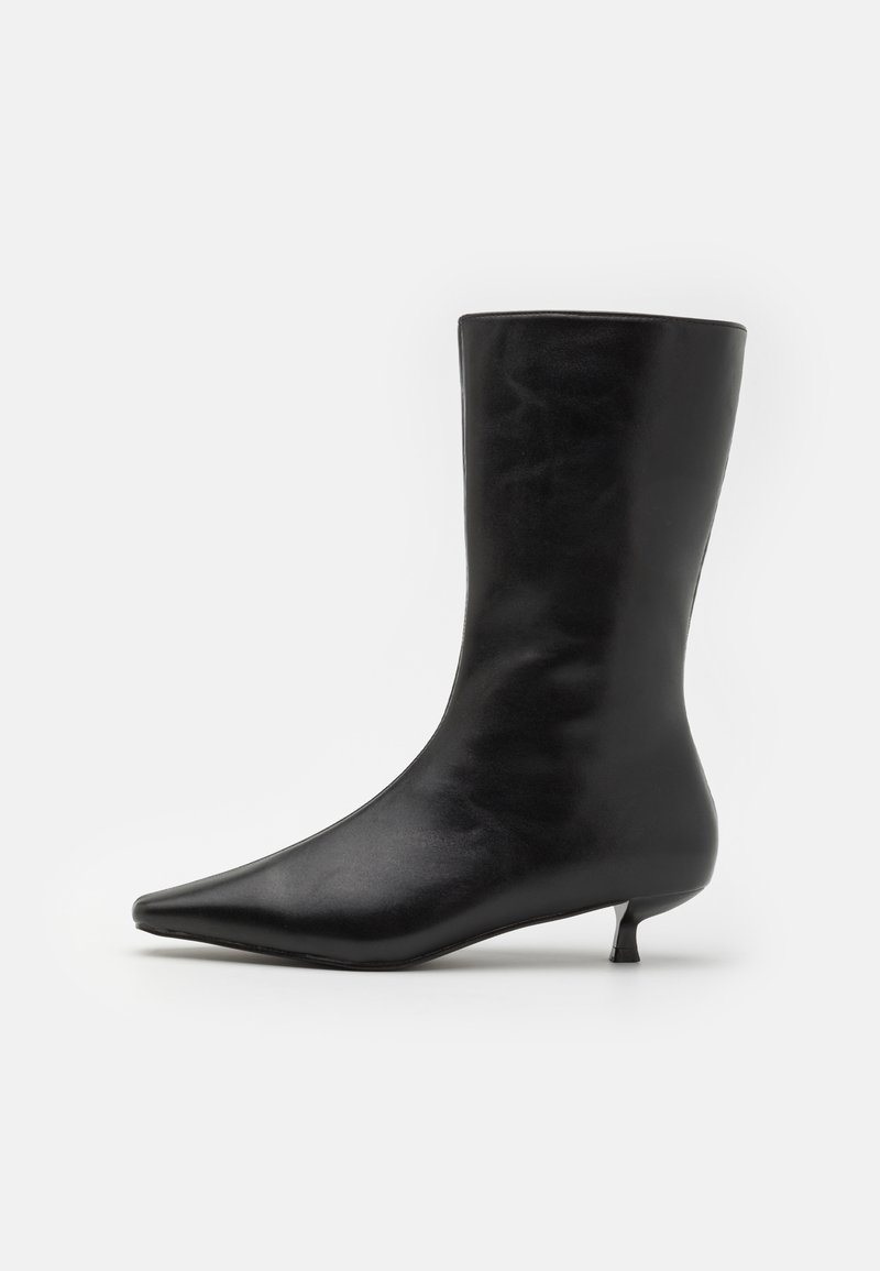 Černá kožená kotníková botka s špičatou špičkou, elegantním svrškem a krátkým širokým podpatkem. Hladká textura s lesklým povrchem.