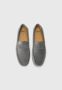 Mocasines de ante gris con un detalle de costura y diseño de mocasín. Presentan una suela plana y una plantilla con marca. Aptos para uso casual.