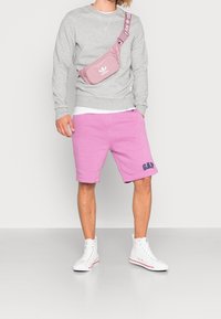 Sudadera gris, pantalones cortos rosas con el logo de GAP y zapatillas altas blancas. La bolsa es rosa con el logo y la correa blanca de Adidas.