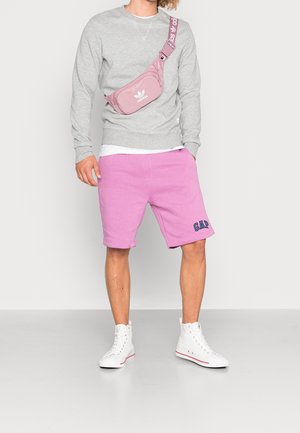 Sudadera gris, pantalones cortos rosas con el logo de GAP y zapatillas altas blancas. La bolsa es rosa con el logo y la correa blanca de Adidas.