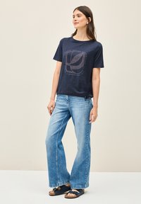 Marineblå bomulds t-shirt med et grafisk design i midten, parret med lyseblå brede jeans og sorte sandaler.