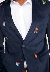 Granatowy blezer z korduroy zdobiony świątecznymi haftami: bałwanek, laska cukrowa, piernik, ostrokrzew, prezent i pomarańcza na przodzie i rękawach.