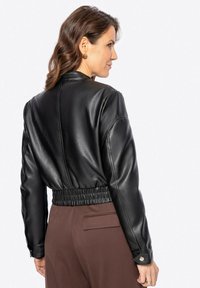 Giacca nera in pelle corta con orlo a costine e maniche lunghe, caratterizzata da una texture liscia e un design minimalista. Accentuata da bottoni a scatto.