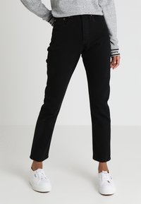 Vaqueros de mezclilla negra con corte recto, cintura alta y diseño de cinco bolsillos. Combinados con zapatillas blancas y un sudadera gris.