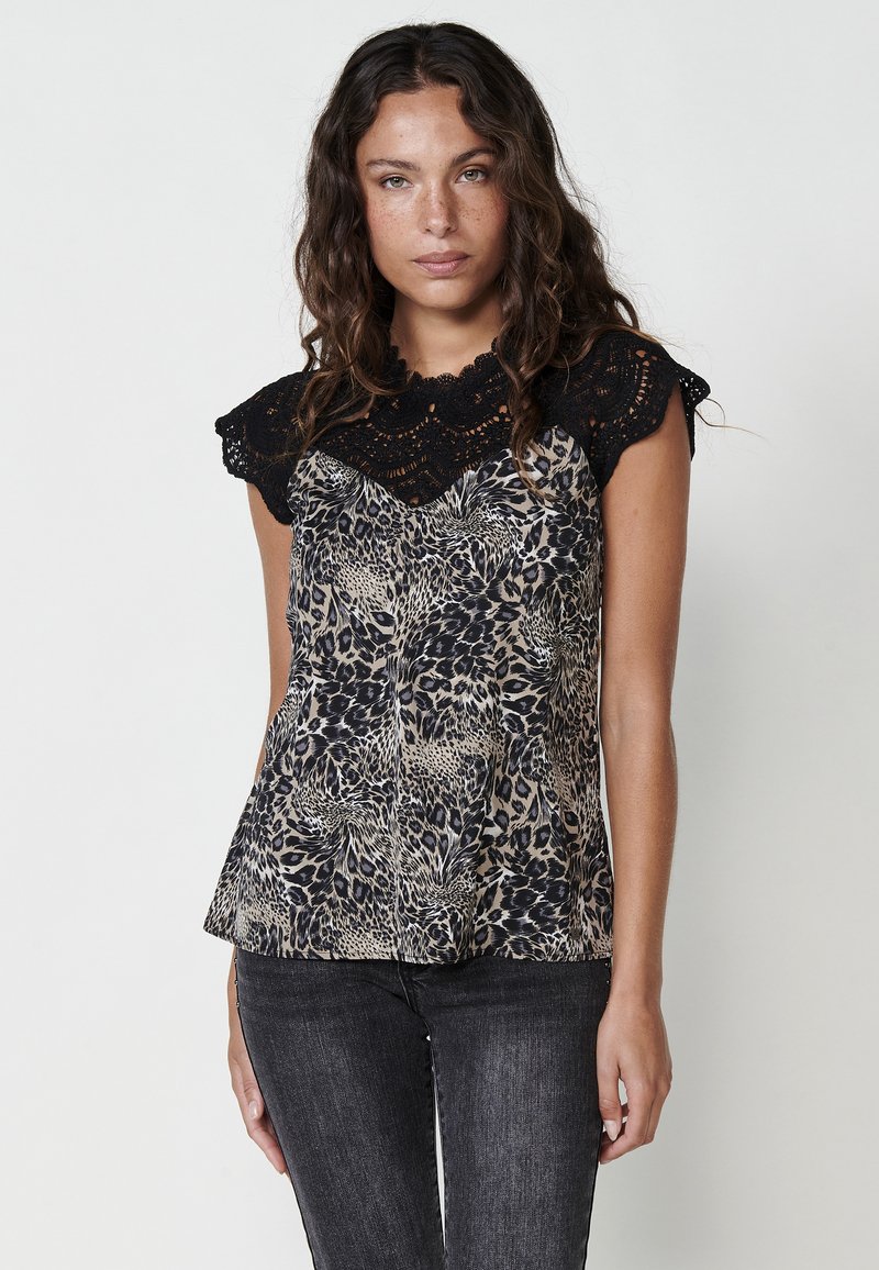 Top senza maniche in pizzo nero con un design a stampa animale beige. Il tessuto appare leggero con una vestibilità svolazzante.