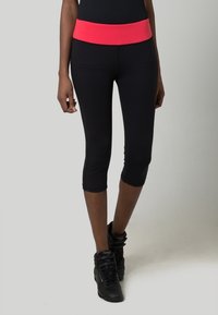 Leggings noirs raccourcis avec une large ceinture élastique rose, fabriqués en tissu extensible, adaptés pour les activités sportives.