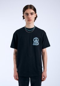 Camiseta de algodón negra con un diseño gráfico azul en el lado izquierdo del pecho. Mangas cortas, corte relajado y una textura suave.