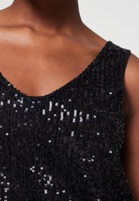 Top de lentejuelas negras con escote en V, diseño sin mangas y una textura suave con patrones de lentejuelas variados que reflejan la luz.