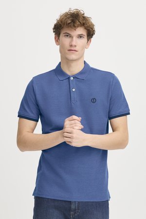 Blå polo skjorte i et struktureret stof med krave, tre-knaps placket og kontrastfarvet marineblå kant på ærmerne. Har et lille emblem.