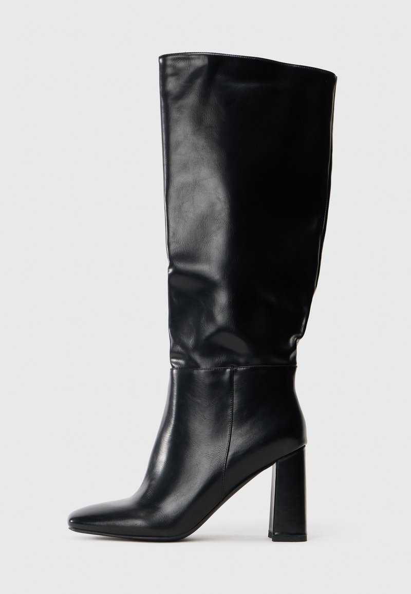 Fekete, térd fölé érő bőr csizma, hegyes orral és magas blokk sarkával, profilból bemutatva fehér háttér előtt.