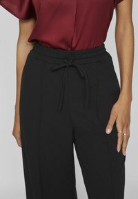 Pantalons larges noirs avec une taille élastique et un cordon de serrage, dotés de poches latérales et d'un tissu lisse et texturé.