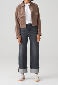 Brown suede cropped jacket with two front pockets, paired with high-waisted dark gray wide-leg jeans, featuring rolled cuffs and white sneakers.