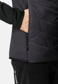 Giacca nera isolante con design trapuntato e tasca laterale con zip. Presenta una texture liscia e cuciture a contrasto lungo la cucitura.