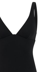 Top de bañador de tela negra texturizada con escote en V profundo y tirantes anchos, sobre un fondo blanco.