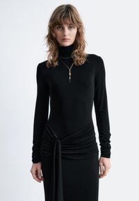 Schwarzes langärmliges Kleid mit hohem Kragen, das ein verdrehtes Design in der Taille und fließenden Stoff aufweist. Glatte Textur überall.