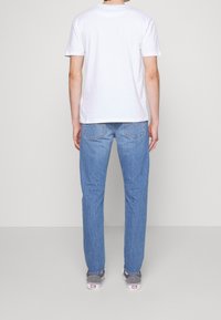 T-shirt en coton blanc, jeans en denim bleu clair, coupe droite avec une légère décoloration, portés avec des baskets en toile grises à semelle blanche.