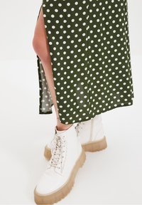 Jupe verte à pois avec une fente latérale, associée à des bottines blanches à lacets avec une semelle transparente épaisse.