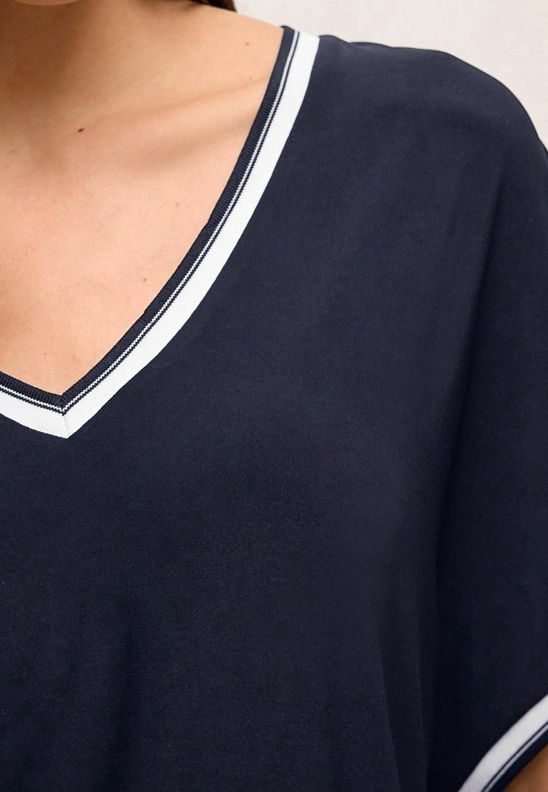 Gros plan sur une personne portant un t-shirt bleu marine à col en V avec un bord rayé blanc et bleu marine le long de l'encolure et du bord de la manche.