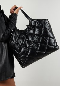 Black quilted tote bag featuring a glossy texture, two sturdy handles, and a star-shaped charm attached to the handle.