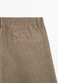 Braune Leinenhose mit elastischem Bund und einer einzelnen Paspeltasche auf der rechten Rückseite.
