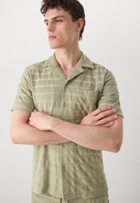 Light green, short-sleeve shirt made of textured fabric with horizontal stripes. Features a chest pocket and button front closure.
