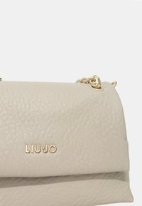 Sac à main en cuir beige clair avec une finition texturée, dotée de quincaillerie dorée et du nom de la marque "LIU JO" embossé sur le devant.