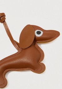 Καφέ δερμάτινο αναμνηστικό σε σχήμα ντάτσχουλντ με μεγάλα αυτιά, λευκό και μαύρο μάτι και ραμμένες λεπτομέρειες. Περιλαμβάνει κρίκο για προσάρτηση.