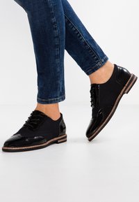 Schwarze Oxford-Schuhe aus einer Mischung von Lackleder und Stoff, mit Schnürdesign, runder Zehenform und einer niedrigen braunen Sohle.