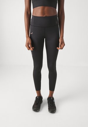 Schwarze hoch taillierte Leggings mit glatter Textur, ausgestattet mit einer seitlichen Tasche und dezenten Branding, kombiniert mit schwarzen Sportschuhen.