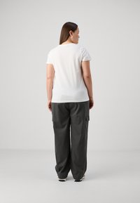 T-shirt blanc à manches courtes associé à un pantalon cargo gris foncé ample avec des poches latérales et une coupe droite.