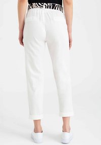 Białe lniane spodnie z podwiniętym mankietem, z czarnym i kremowym paskiem w zwierzęcy wzór. Gładki kolor, luźny krój, gładka tekstura.