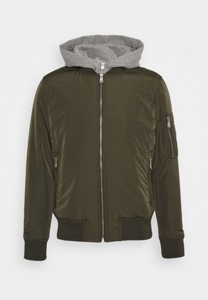 Veste bomber vert olive avec une fermeture éclair argentée sur le devant, poches latérales, poche zippée sur la manche et capuche grise attachée avec cordons.