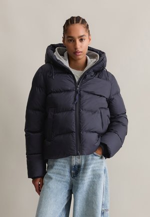 Giacca puffer blu navy con cappuccio, chiusura con zip e tasche laterali; presenta sezioni trapuntate e un cappuccio foderato in grigio per un ulteriore calore.
