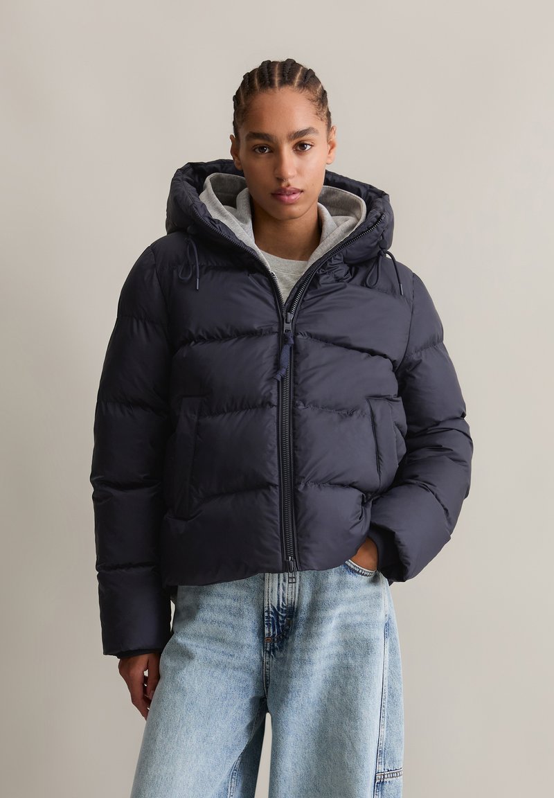 Navy puffer jacket with a hood, zip closure, and side pockets; features quilted sections and a gray lined hood for added warmth.