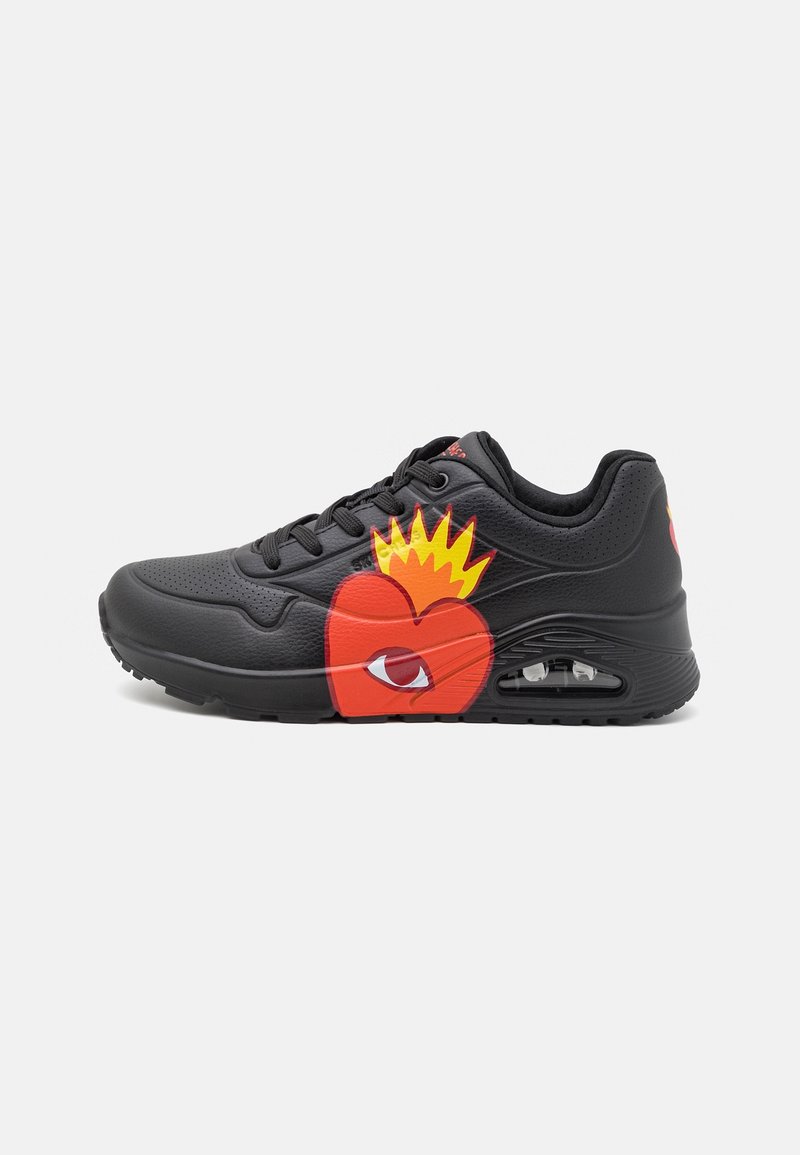 Baskets noires avec un cœur rouge et un graphisme de flamme jaune, avec une semelle à coussin d'air visible et des lacets noirs.