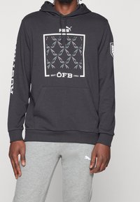 Felpa grigia scura in misto cotone, con stampa grafica in bianco e teal, tasca a canguro e polsini a coste. Logo sulla manica.