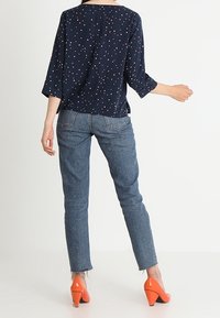 Blusa blu navy con pois bianchi e rosa, maniche tre quarti; abbinata a jeans azzurri e décolleté arancioni.