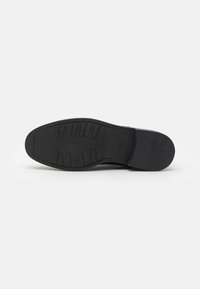Suela de zapato de goma negra con un patrón de agarre texturizado que presenta estrías verticales y horizontales, bordes curvados y un diseño plano.