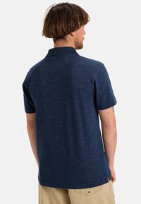 Polo blu navy a maniche corte, con una texture sottile e colletto. Fessure laterali sull'orlo per facilitare i movimenti.