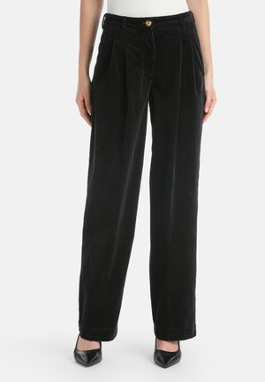 Zwarte corduroy broek met een wijduitlopende pasvorm, voorzien van plooien, een knoopsluiting en een gestructureerde stof. Gepaarde met scherpe zwarte hakken.