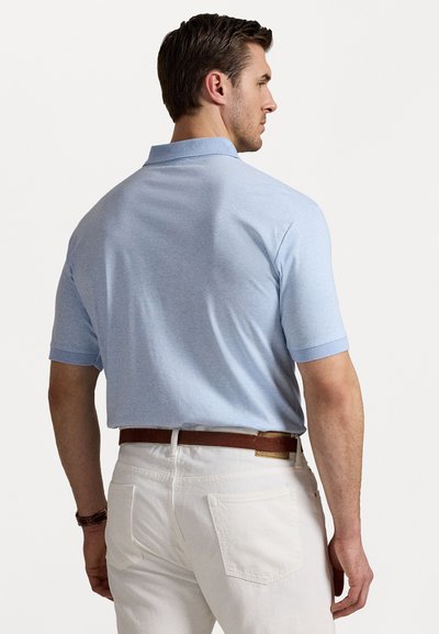 Polo de culoare albastru deschis, cu mâneci scurte, realizat dintr-un material neted. Purtați cu pantaloni albi și o curea maro, evidențiind un stil casual.