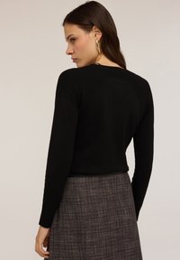 Svart långärmad topp med ribbad textur vid axlarna, med en figurnära design. Bärs med en texturerad grå kjol.