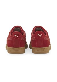 Zapatillas de gamuza roja con suela de goma texturizada, parche de logo en la parte trasera y acentos de costura blanca. Presenta un diseño de perfil bajo.