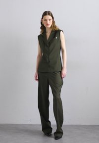 Blazer sem mangas na cor verde-azeitona, com colarinho serrado, fecho de botão e calças ajustadas a condizer. Textura suave com silhueta ajustada.