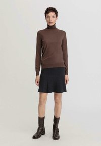 Un pull à col roulé en laine marron associé à une jupe évasée en tricot côtelé foncé. Des bottes en cuir marron à cheville complètent la tenue.