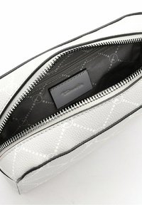 Pochette en cuir blanc texturé avec une fermeture éclair argentée partiellement ouverte, montrant une doublure en tissu noir avec un motif circulaire subtil et une petite étiquette en cuir à l'intérieur.