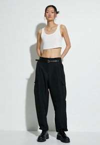 Witte geribbelde crop top, zwarte cargo-broek met zijzakken, zwarte riem met ronde gesp, en chunky zwarte veterschoenen.